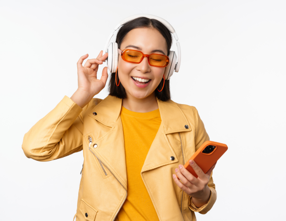 happy-stylish-asian-woman-sunglasses-listening-music-headphones-holding-smartphone-singing-dancing-standing-white-background 1